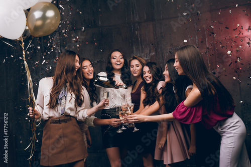 Beautiful girls celebrate New Year. Enjoying carefree time together. Group of beautiful young girl throwing gold confetti and looking happy and drinking champagne