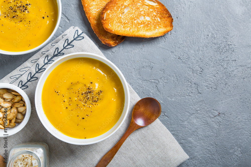 Roasted pumpkin and carrot soup with black pepper and pumpkin seeds on grey concrete background. Close up. Top view. Copy space Roasted pumpkin and carrot soup with black pepper and pumpkin seeds on grey concrete background. Close up. Top view. Copy space