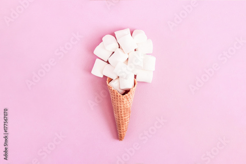 Creative minimal still life on pastel pink colored background. Waffle cone with marshmallow sweets. Copy space for text