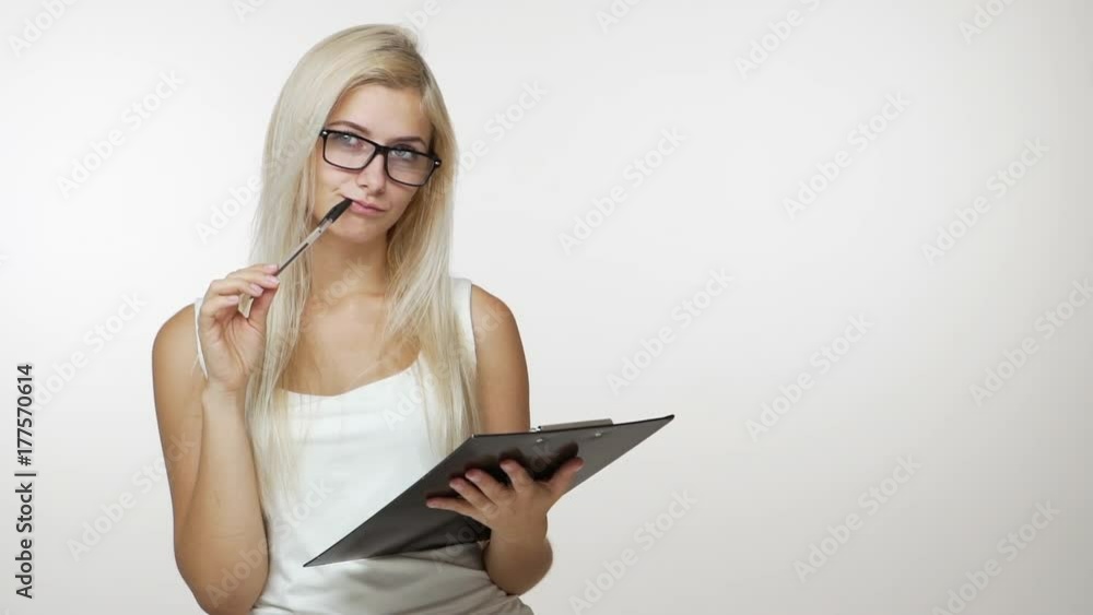 slomo copy space picture of blond woman in office looking at clipboard examining documents thinking hard holding pen near mouth over white background. Concept of emotions slomo copy space picture of blond woman in office looking at clipboard examining documents thinking hard holding pen near mouth over white background. Concept of emotions