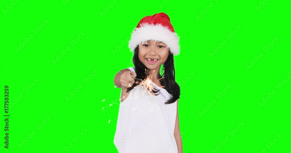 Cheerful toothless little girl wearing a Santa hat while playing firework or burning sparkler in the studio, shot in 4k resolution with green screen background Cheerful toothless little girl wearing a Santa hat while playing firework or burning sparkler in the studio, shot in 4k resolution with green screen background