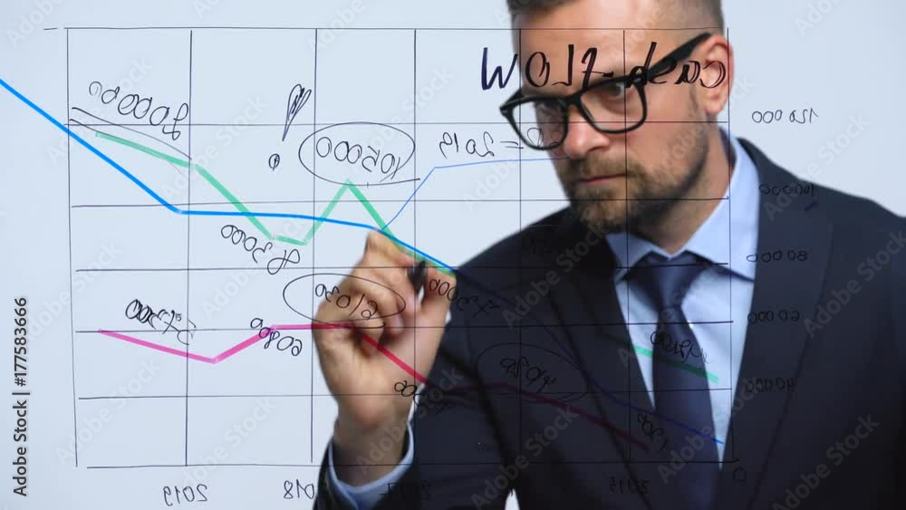 Man draws various growth charts, calculating prospects for success in a modern glass office Man draws various growth charts, calculating prospects for success in a modern glass office