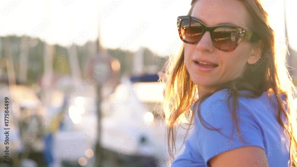 Woman in sunglasses walking along the dock with a lot of yachts and boats at sunset, close up Woman in sunglasses walking along the dock with a lot of yachts and boats at sunset, close up