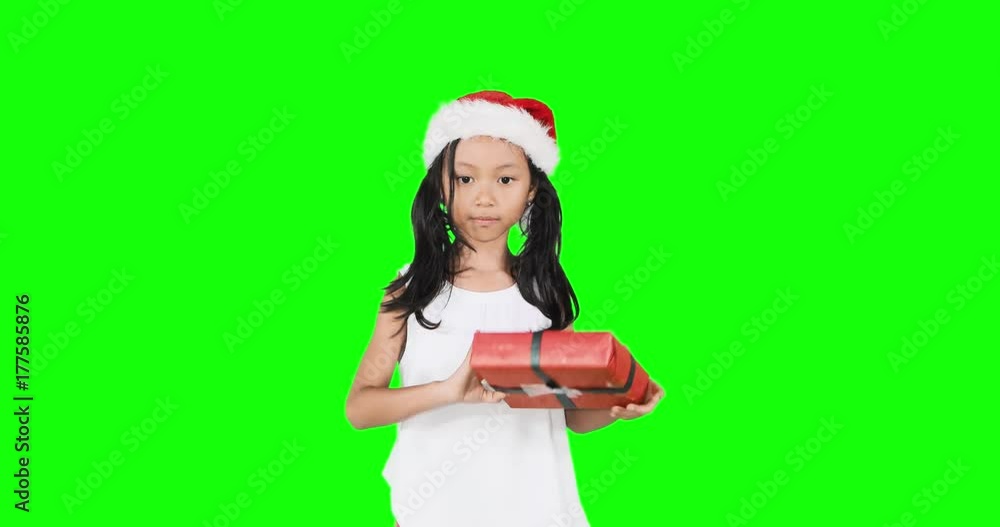 Curious little girl shaking a Christmas gift while wearing a Santa hat and looks happy, Shot in 4k resolution with green screen background Curious little girl shaking a Christmas gift while wearing a Santa hat and looks happy, Shot in 4k resolution with green screen background