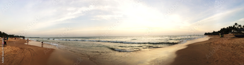A panoramic view of the sun drenched beach and people playing in the water A panoramic view of the sun drenched beach and people playing in the water