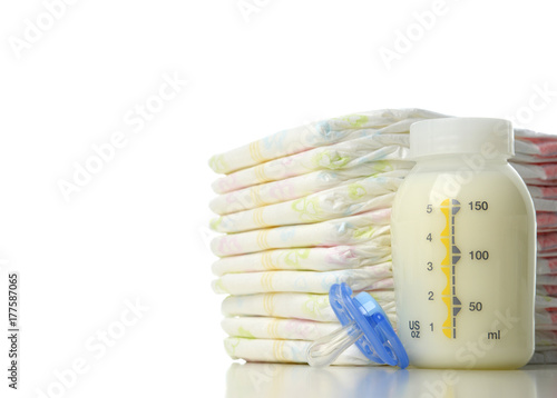 New born child stack of diapers nipple soother and baby feeding bottle with milk 