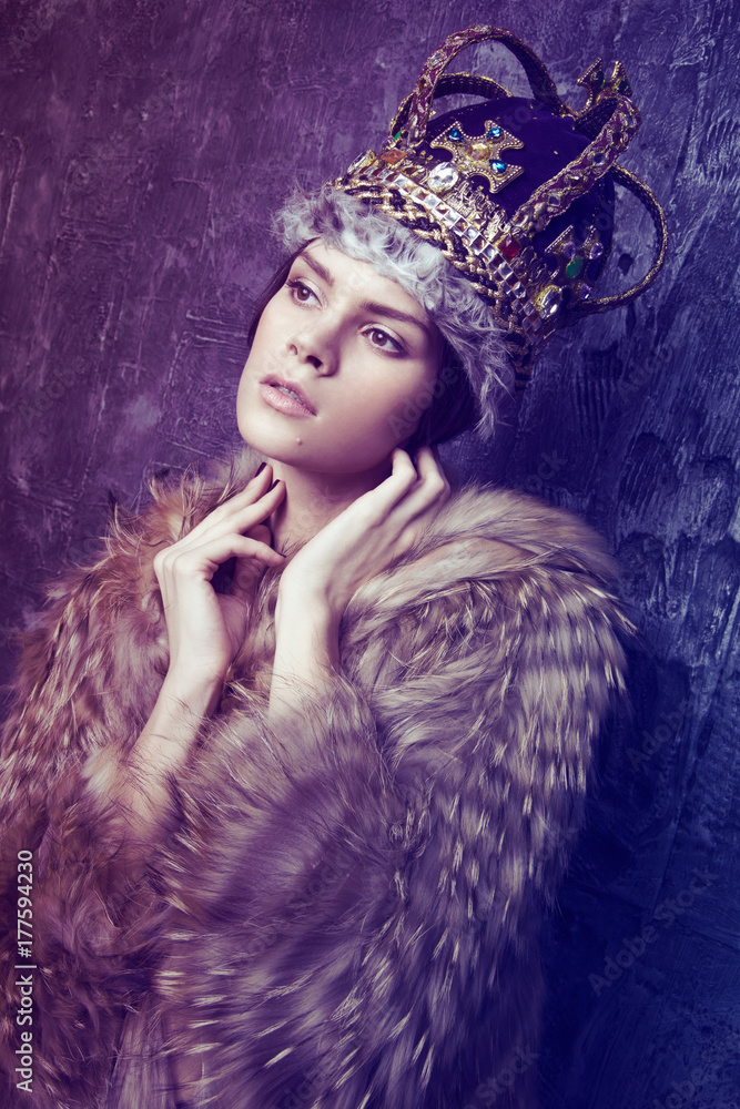 Studio shot of beautiful young woman in crown and fur coat at dark studio background Studio shot of beautiful young woman in crown and fur coat at dark studio background
