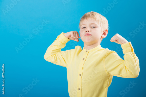 Bild auf Leinwand Charming small caucasian boy showing muscle on yellow background