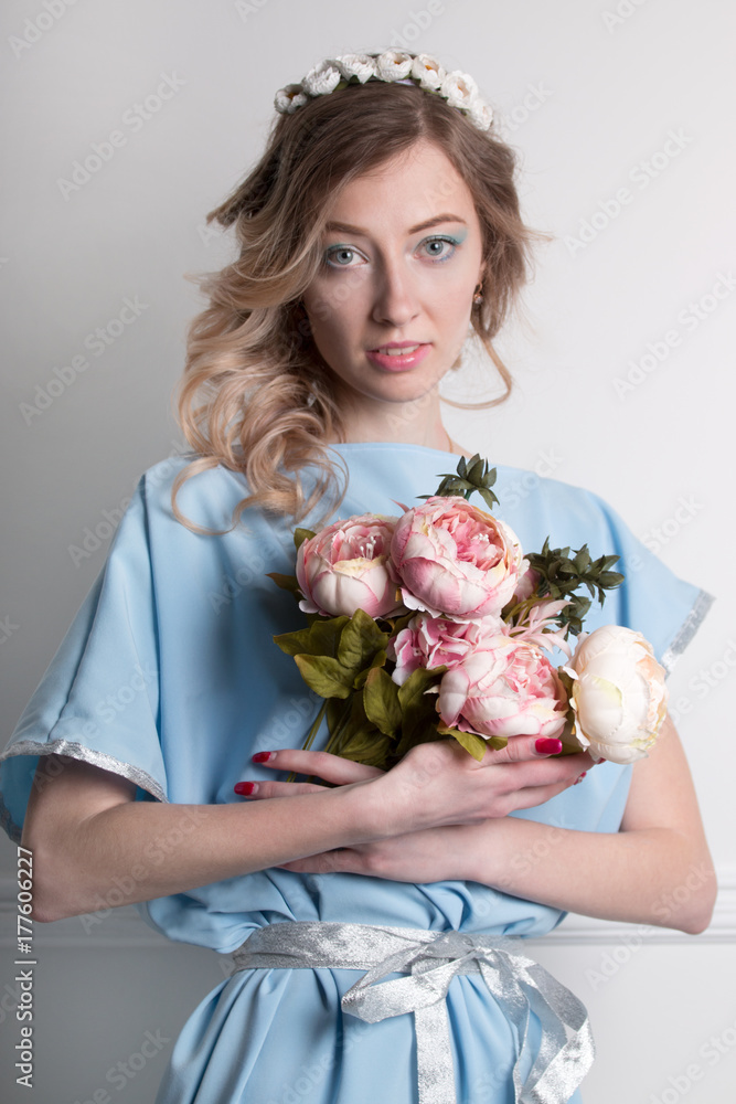 Beautiful young blonde woman with clean skin and flower wreath in her hair on grey background with bouquet of flowers Beautiful young blonde woman with clean skin and flower wreath in her hair on grey background with bouquet of flowers