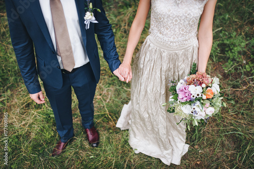 Bride and groom holding hands with flowers wedding bouquet.