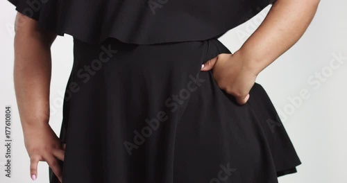 Confident strong young plus size African American model wearing a black short twirly dress flirting with camera isolated on white. tilt movement of camera