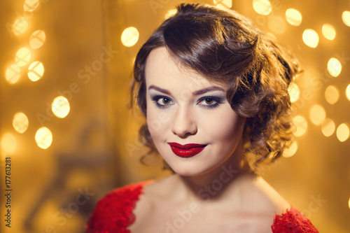 Brunette woman in red dress in luxury interior. Christmas tree. Presents and gift boxes under it. New Year decorations.