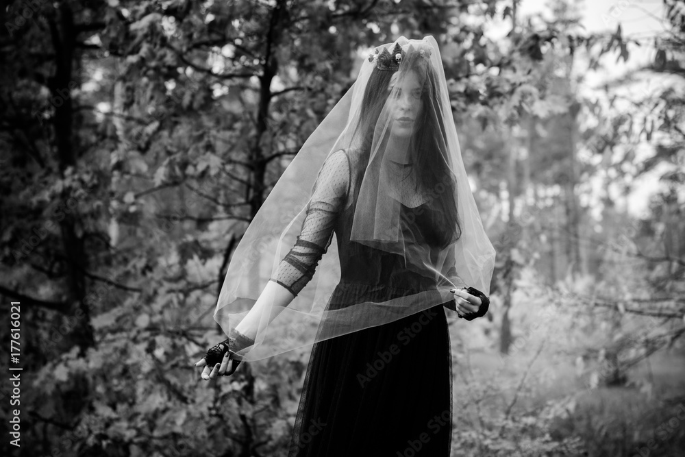 Halloween Witch with magic lights in dark autumn forest. Beautiful young european or american woman in black Gothic dress.Halloween party at city, decor and design for party, mysterious lady in woods Halloween Witch with magic lights in dark autumn forest. Beautiful young european or american woman in black Gothic dress.Halloween party at city, decor and design for party, mysterious lady in woods