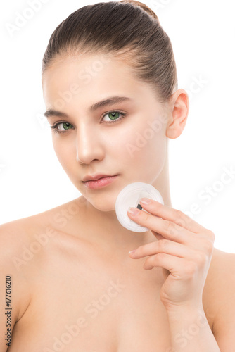 Young girl cares for face skin relaxation. Beautiful young brunette woman with clean perfect fresh skin using cotton pad. Youth and skin care concept. Isolated on a white.