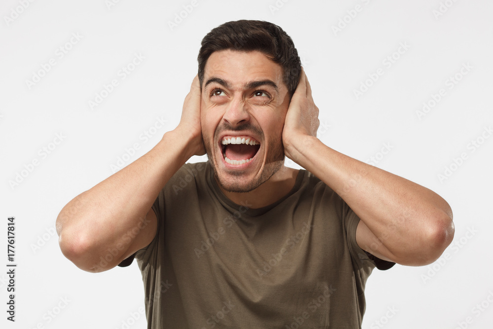 Young handsome man shout at noisy neighbours, stressed by noise, closing ears with both hands, avoid listening fight Young handsome man shout at noisy neighbours, stressed by noise, closing ears with both hands, avoid listening fight