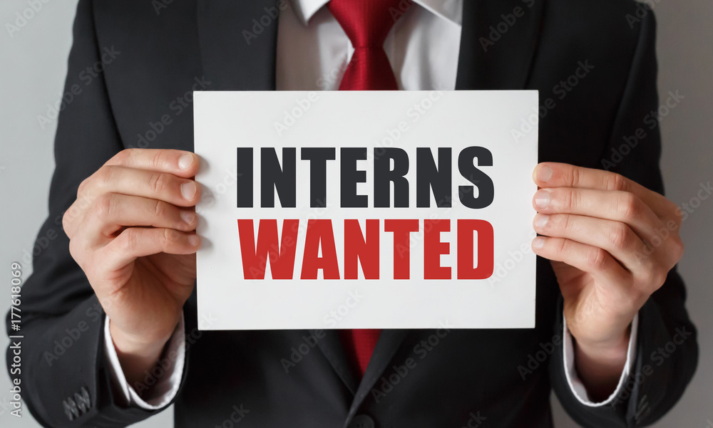 Businessman holding a card with text Interns Wanted Businessman holding a card with text Interns Wanted