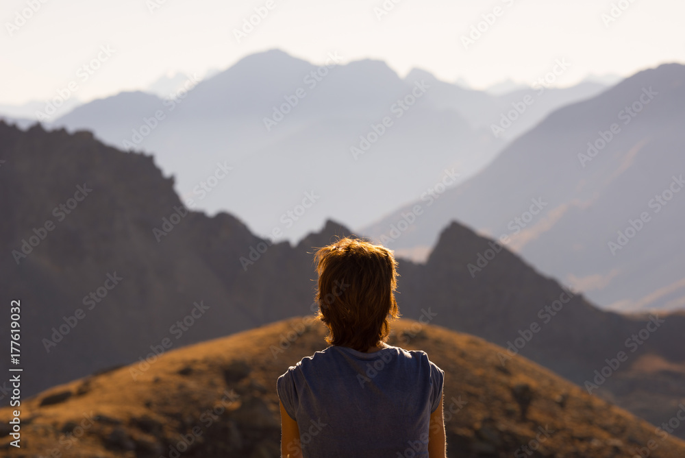One person looking at view high up on the Alps. Expasive landscape, idyllic view at sunset. Rear view.