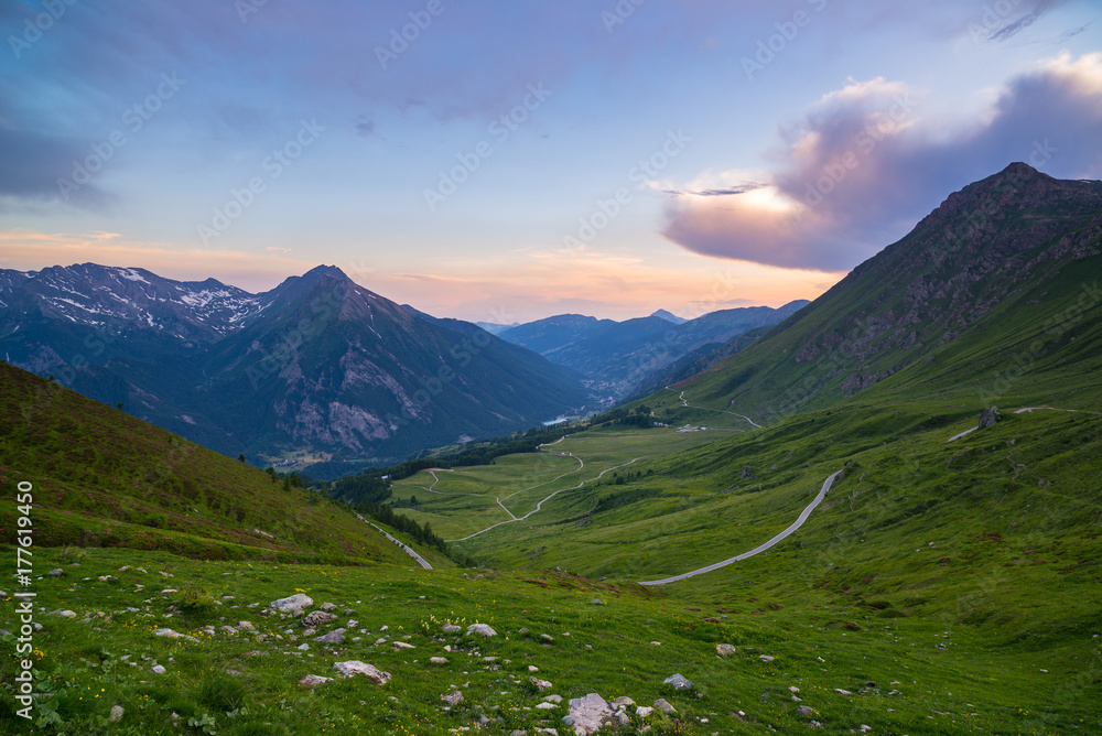 Mountain road leading to high mountain pass on the Italian Alps.. Expasive view at sunset, colorful dramatic sky, adventure road trip in summer.