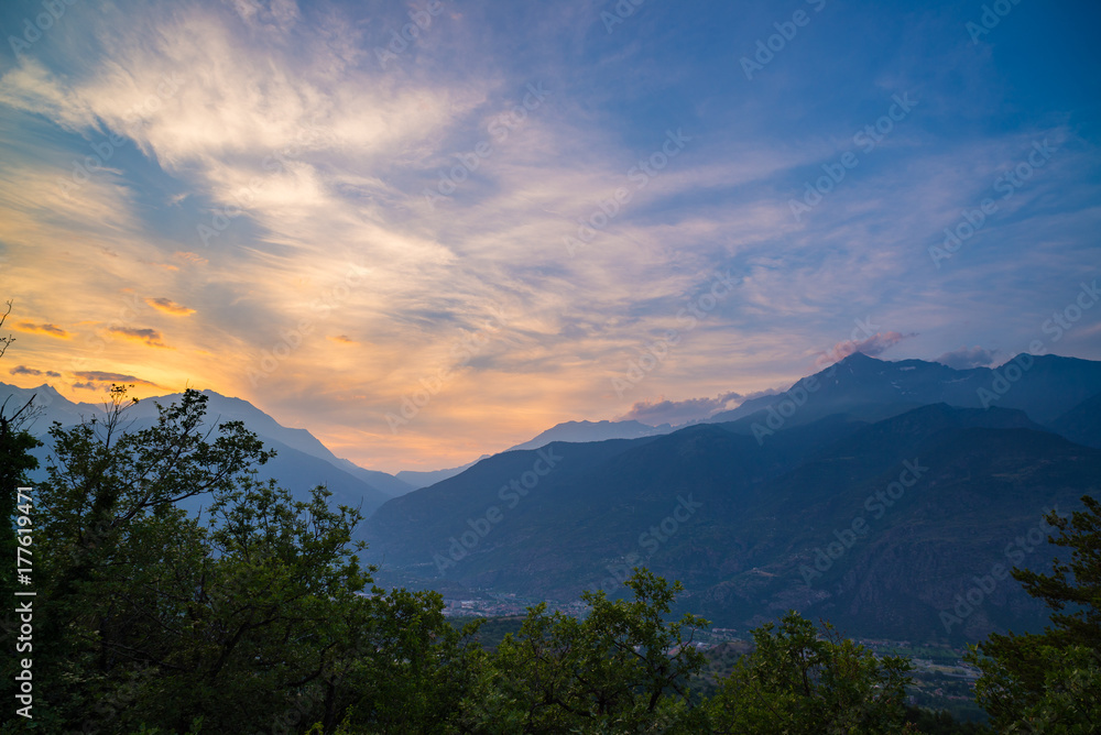 The Italian Alps at sunset. Summer colorful sky over the majestic mountain peaks, woodland and green valleys.