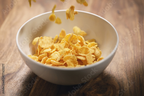 corn flakes falling into white bowl on table closeup