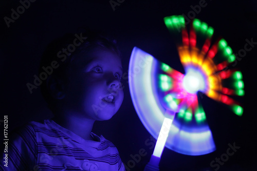 A small boy in the darkness enthusiastically looks at a bright glowing toy. Experiment with light and rotation. A boy with a magic wand - a little wizard