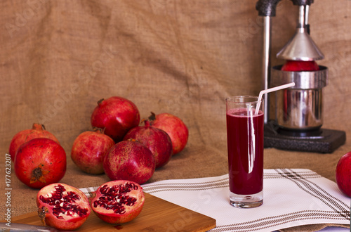 Pomegranate juice in a glass next to a cut pomergranat on a board. Metal juicer press behind. photo