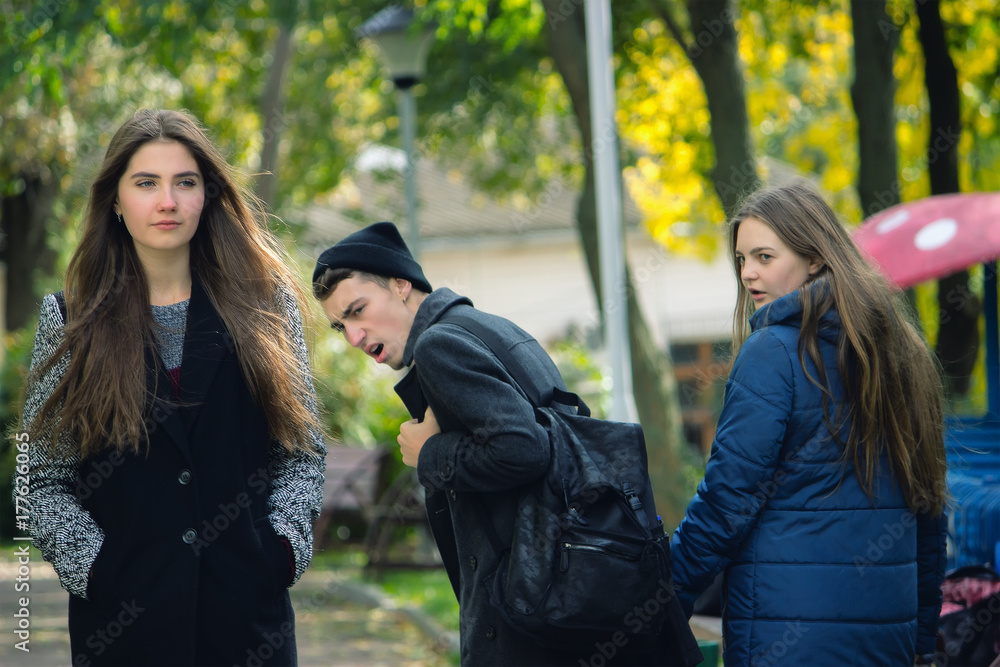 Fototapeta premium Disloyal man walking with girlfriend and looking amazed at another seductive girl