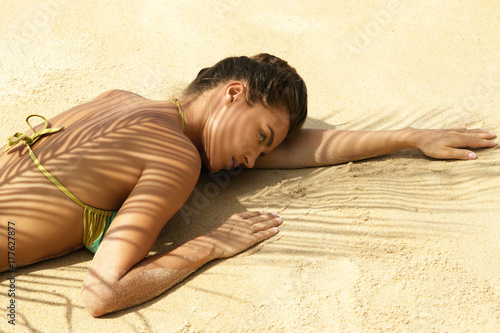 Woman is lying on the beach under palm leaf