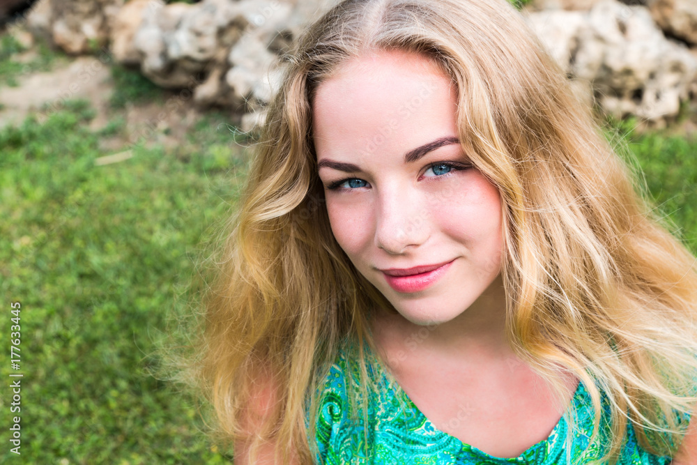 Naklejka premium Cute blonde teenager girl in a park in a summer day