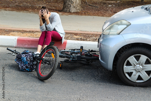 A woman holding her head near a traffic accident between electric bicycle and car