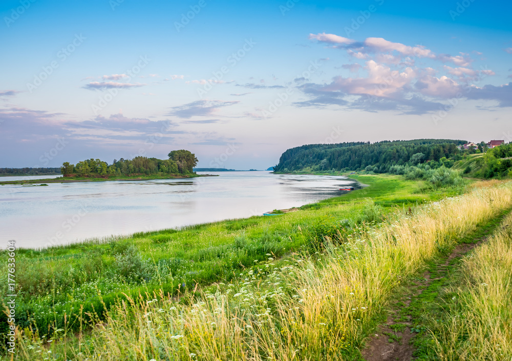 The Kama River in Udmurtia, Russia. Thick grass along the shore. The island overgrown with wood on the river