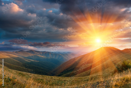 Panoramic landscape of fantastic sunset in the mountains. View of the autumn hills lit by the rays of the evening sun. Dramatic clouds over sky.