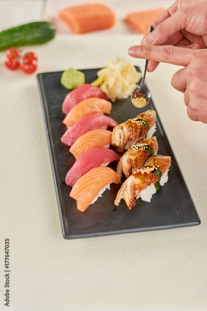 Chef putting sesame on nigiri sushi. Cook preparing appetizing sushi at kitchen. Delicious sushi on plate. Chef putting sesame on nigiri sushi. Cook preparing appetizing sushi at kitchen. Delicious sushi on plate.