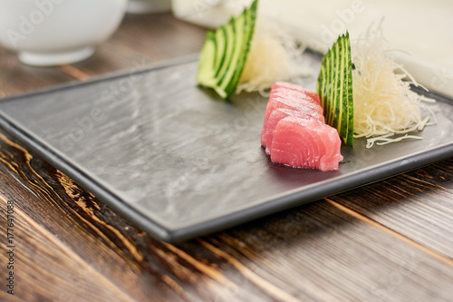 Tuna and cucumber on plate for sushi. Preparing of sashimi from tuna at professional kitchen. Ingredients for sushi on wooden table.