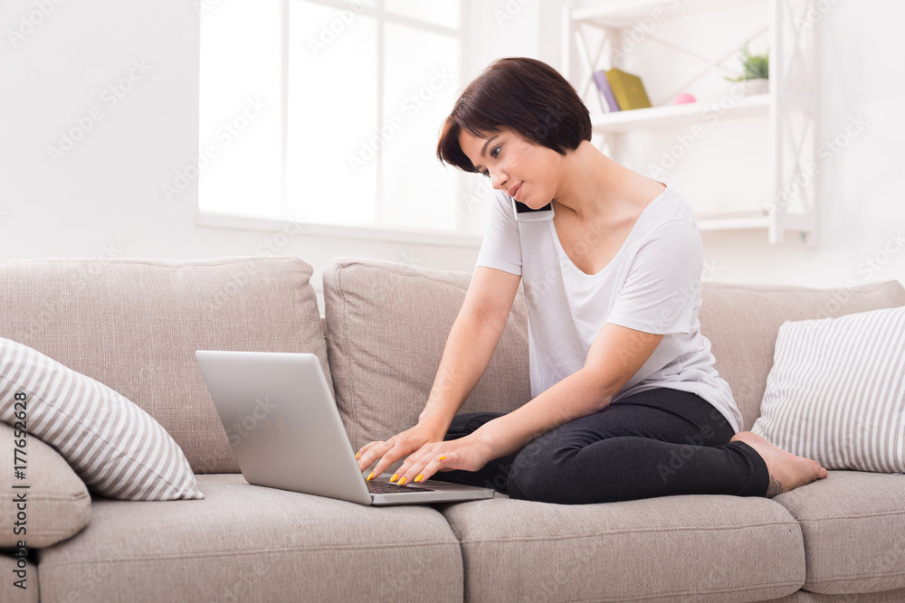 Pensive girl with laptop and mobile sitting on beige couch Pensive girl with laptop and mobile sitting on beige couch