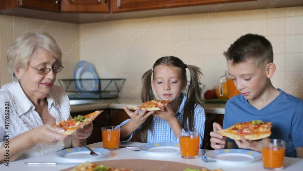 Grandmother with grandchildren are eating pizza at home Grandmother with grandchildren are eating pizza at home