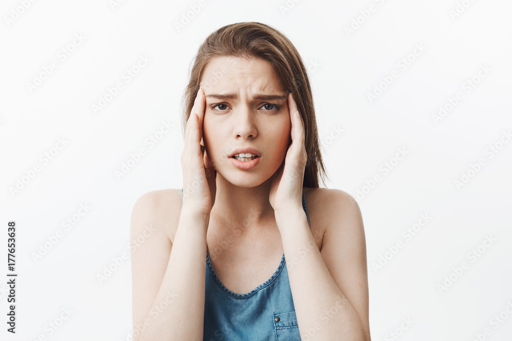Portrait of suffering young attractive caucasian student girl with dark long hair in blue shirt massaging forehead with fingers, looking in camera with tired expression after long day at work Portrait of suffering young attractive caucasian student girl with dark long hair in blue shirt massaging forehead with fingers, looking in camera with tired expression after long day at work