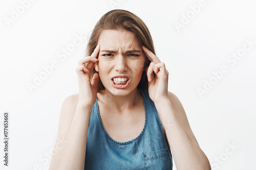 Beautiful young charming dark-haired european woman squeezing forehead with fingers, looking in camera with unhappy expression, suffering from terrible headache after listening to loud music in