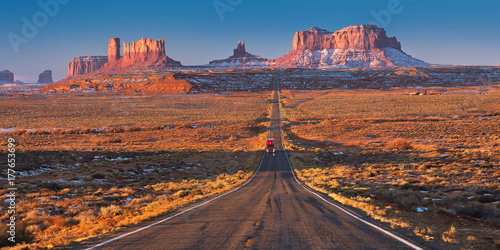 Bild auf Leinwand Red car driving on a straight road in Monument Valley early on a Sunny morning