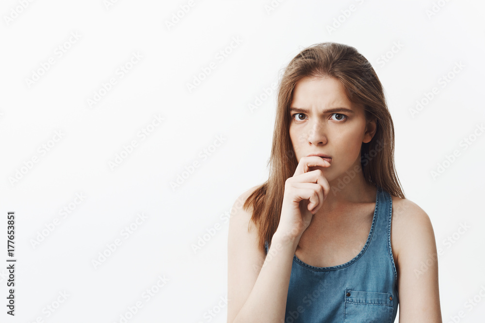 Close up of handsome charming young european woman with long dark hair in casual blue clothes holding hand near lips, looking in camera with thoughtful face expression trying to rember name of person Close up of handsome charming young european woman with long dark hair in casual blue clothes holding hand near lips, looking in camera with thoughtful face expression trying to rember name of person