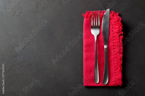 Festive set of knife and fork on a red napkin on a dark stone slate background, top view, copyspace