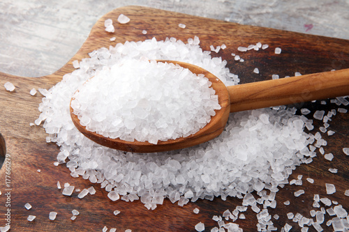sea salt with wooden spoon and crystals of salt on wooden background.