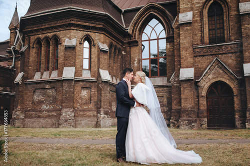 The bride blond and groom are standing on the background of the catalytic church. Catholic temple. Wedding concept.