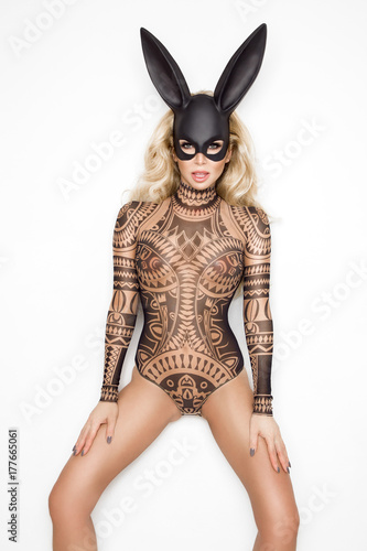 Beautiful young woman in Halloween, tattoo costume and black bunny  mask, standing on white background