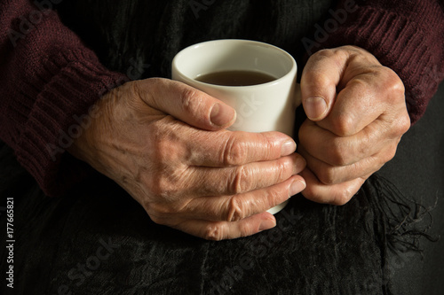 Old woman warming her wrinkled hands with a mug of coffee