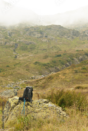 A view of a mountain valley covered with clouds. In the foreground on the stone is a backpack, to the stone are propped poles for the nordic walk
