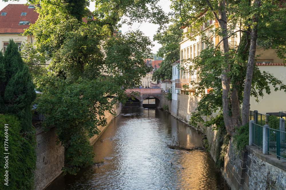 Old buildings, verdant trees, bridge and water canal on the Kampa Island in Prague, Czech Republic on a sunny day in the summer.