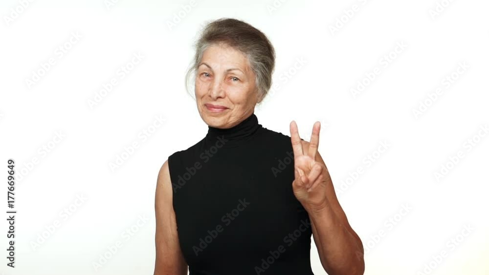slow motion joyful older lady with grey tied hair looking at camera smiling with white teeth showing victory sign over white background. Concept of emotions slow motion joyful older lady with grey tied hair looking at camera smiling with white teeth showing victory sign over white background. Concept of emotions