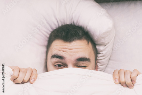 A young man wakes up in the morning under a blanket.