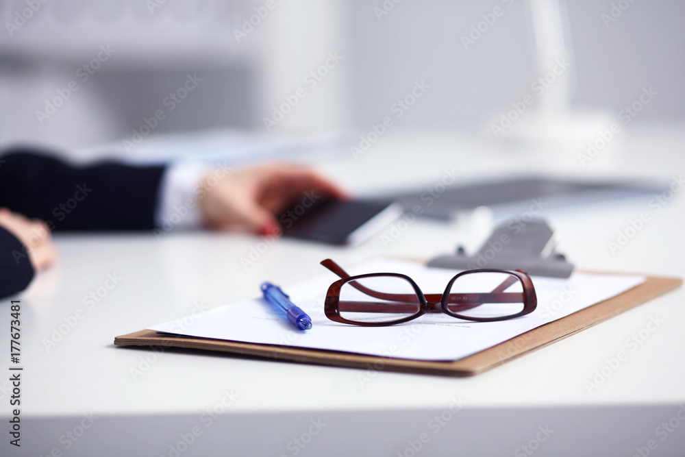 Businesswoman using her phone in office sitting on desk, selective focus Businesswoman using her phone in office sitting on desk, selective focus